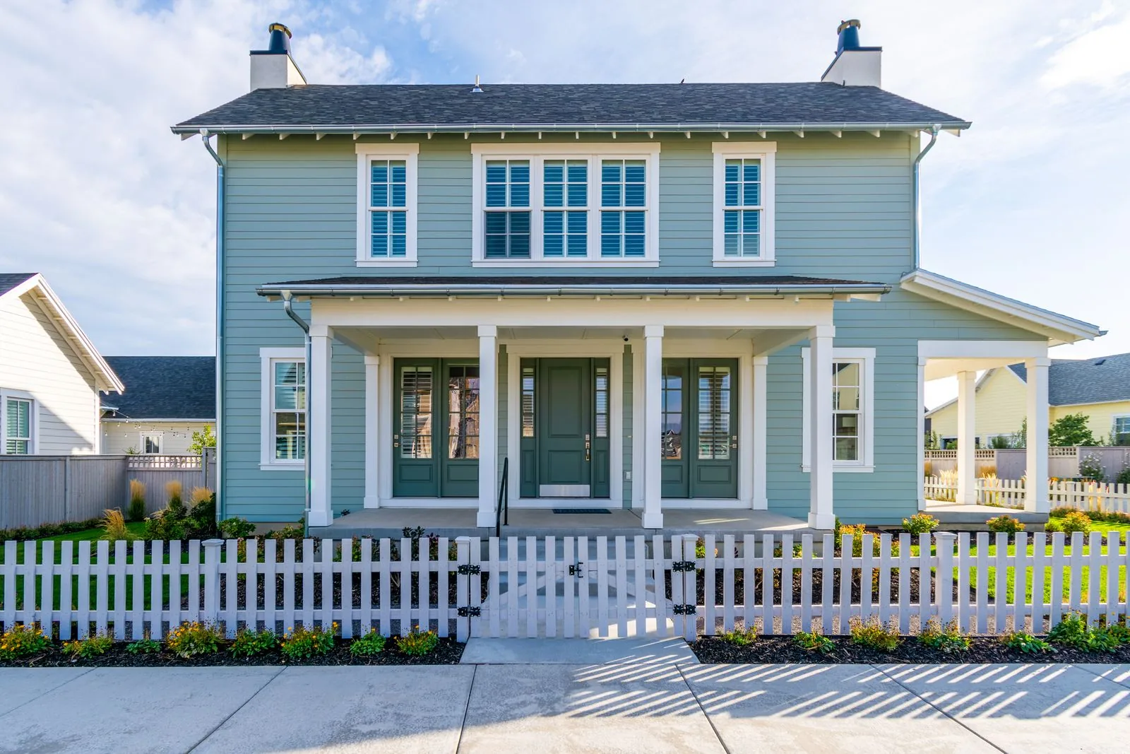 Sage-green craftsman home with white-trimmed casement windows and a white picket fence