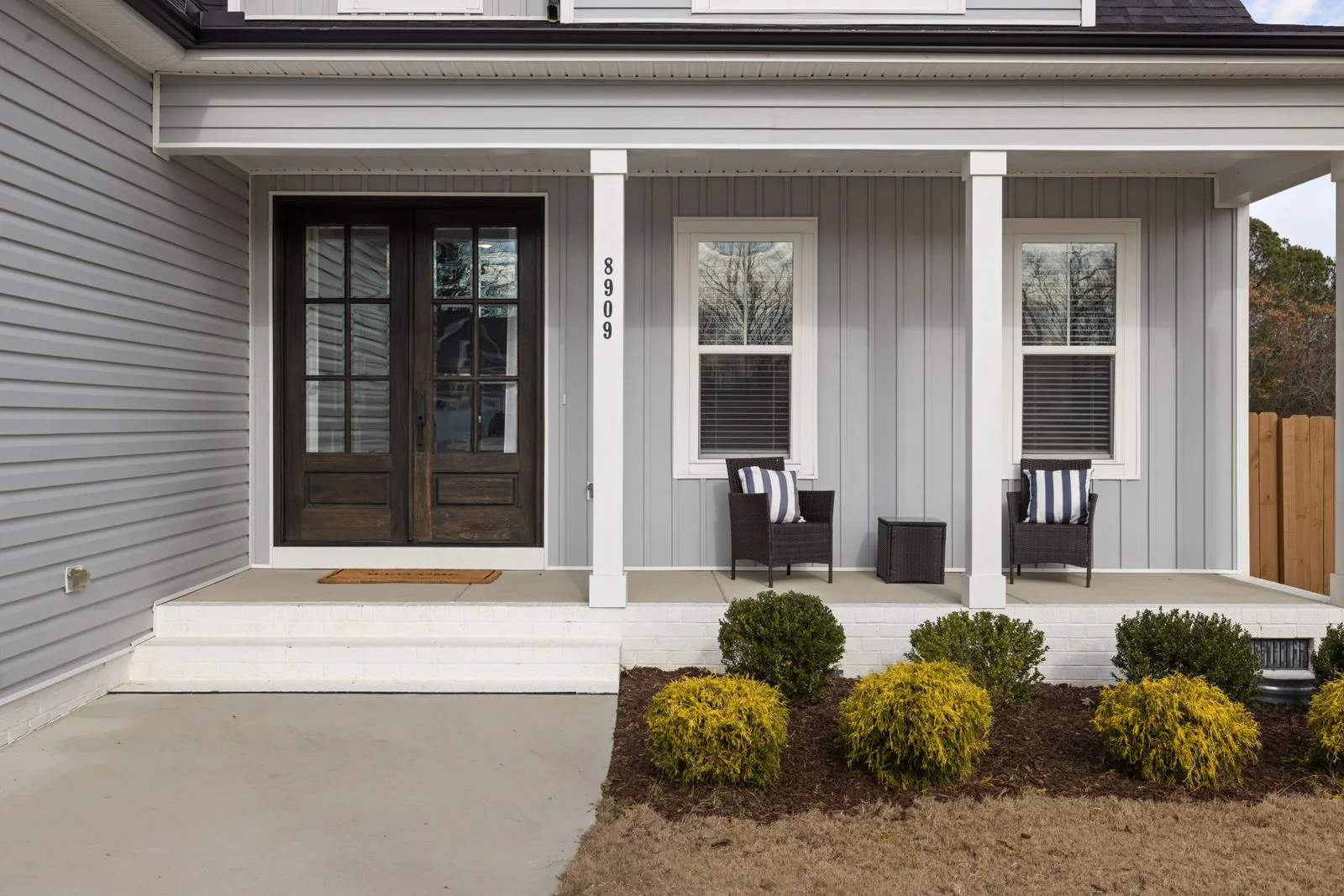 Dark wood front door with glass panes on a gray-sided house with a covered porch