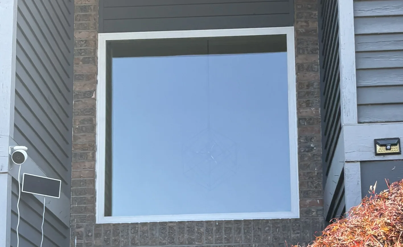 Large white fixed picture window above a front door on a brick and gray-sided home